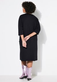 Vestido negro con mangas tres cuartos, que presenta un corte holgado y un dobladillo que llega a la mitad de la pantorrilla. Combinado con botas vaqueras metálicas rosas.
