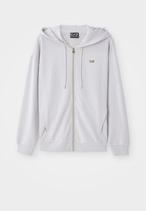 Helle graue Zip-Hoodie aus weichem Material, mit Kapuze, goldfarbenem Reißverschluss und kleinem Logo auf der Brust. Glatte Textur und lässiger Schnitt.