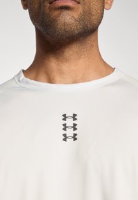 Λευκό αθλητικό t-shirt με στρογγυλ ή λαιμόκοψη, με τρία μαύρα λογότυπα τοποθετημένα κατακόρυφα στο κέντρο του στήθους. Λείο, ελαφρύ ύφασμα.