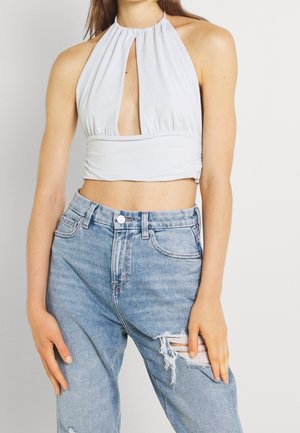 Jasnoszary crop top na halter z detalem w formie otworu z przodu, połączony z wysokim stanem podartymi niebieskimi dżinsami.