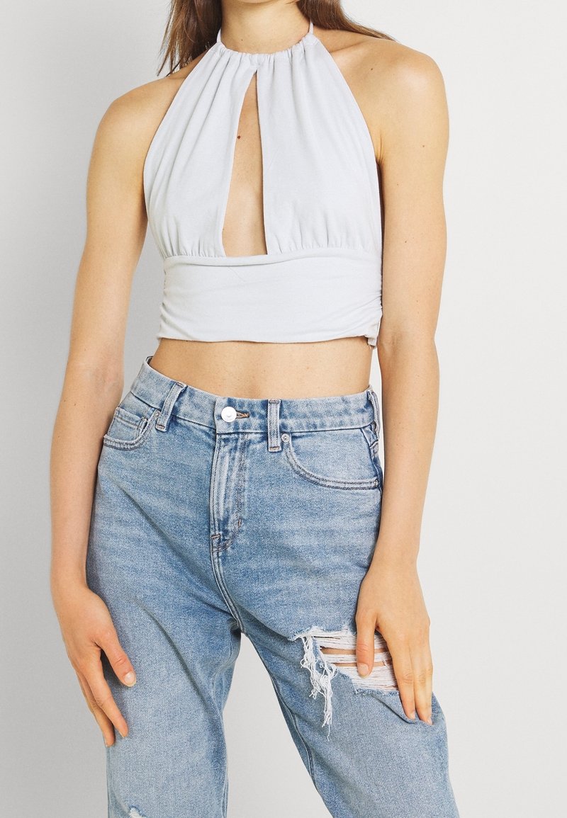 Ljusgrå halterneck crop top med en framkeyhole-detalj, parat med högmidjade slitna blå denimjeans.