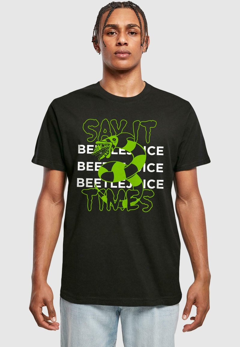 Camiseta negra de algodón con texto verde en negrita, un gráfico de serpiente y un patrón repetido de "BEETLEJUICE". Cuello redondo, mangas cortas, corte relajado.