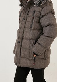 Harmaa toppatakki, jossa on teksturoitu kangas, irrotettava huppu karvareunuksella, läppätaskut ja vetoketjusomisteet. Takissa on vartalonmyötäinen malli.