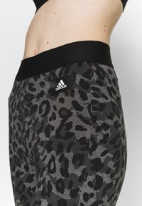 Leggings à imprimé léopard noir et gris avec une taille élastique noire, ornés d'un logo Adidas sur une plaque rectangulaire.