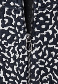 Gros plan sur un tissu à imprimé léopard noir et blanc avec une fermeture éclair en métal noir au centre, partiellement ouverte.