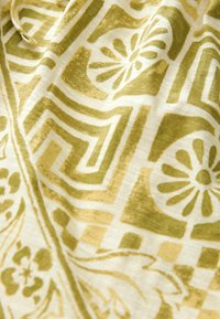 Tissu en coton présentant un fond jaune clair avec des motifs géométriques verts complexes et des motifs floraux, texture douce et éclat subtil.