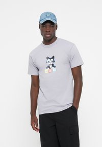 Gray cotton t-shirt featuring a cartoon cat graphic with 'HUF' text in multi-colored blocks. Paired with a denim blue cap.