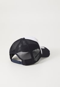 Gorra en blanco y negro con visera curva, parte trasera de malla, cierre a presión ajustable y parche circular con logo en el panel trasero.