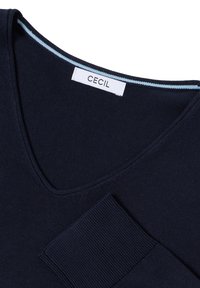 Granatowy sweter z dekoltem w serek, wykonany z dzianiny, z ribbowaną kieszenią i kontrastującym jasnoniebieskim przeszyciem wzdłuż dekoltu.