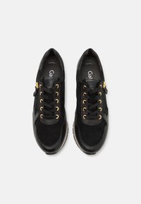 Paire de baskets noires en cuir et en suède avec des œillets et des lacets dorés, vues de dessus sur fond blanc.