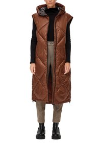 Braune gesteppte ärmellose Pufferweste mit Kapuze und einem durchgängigen Reißverschluss. Getragen über einem schwarzen Rollkragenpullover und karierten Hosen.