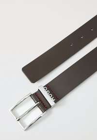 Ceinture en cuir marron avec une boucle en métal argenté. Présente des coutures rouges sur le côté. La boucle est gravée "HUGO". Texture lisse.