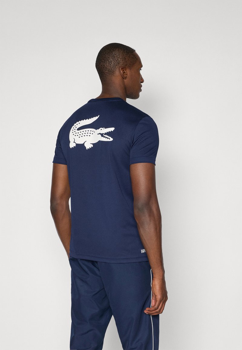 T-shirt blu navy a maniche corte realizzato in tessuto liscio, con una grande grafica di coccodrillo bianco sul retro e un marchio discreto vicino all'orlo.