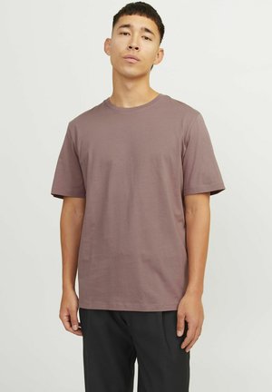 Kurzärmliges T-Shirt mit Rundhalsausschnitt in gedämpftem Mauve, aus weichem Stoff, mit geradem Saum und lockerer Passform; kombiniert mit schwarzen Hosen.