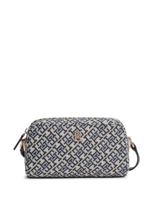 Trousse de toilette rectangulaire avec motif géométrique bleu, fond beige, emblème logo doré, fermeture éclair et anse latérale.