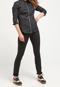 Svart lättvikts zip-up skjorta med ståkrage, kombinerad med svarta tajta byxor och svarta och vita oxfordskor med röda accenter.