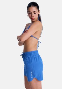 Μπλε σορτς κολύμβησης Roxy με ελαστική μέση, κορδόνι και πλαϊνές τσέπες. Διαθέτει κυματοειδές τελείωμα και λεπτομέρεια με λογότυπο μπροστά.