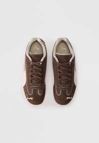 Brown suede sneakers with a light pink accent, textured lace detail, and white stitching. Features a logo on the side and lightly cushioned collar.