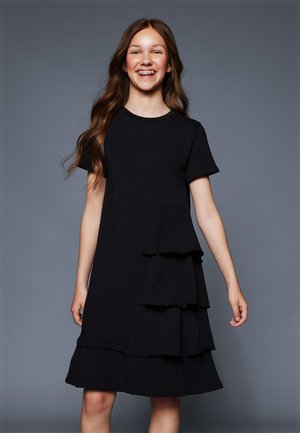 Robe en coton noir avec des manches courtes, un col rond et un détail de volants superposés sur le côté gauche à l'avant. Texture lisse.