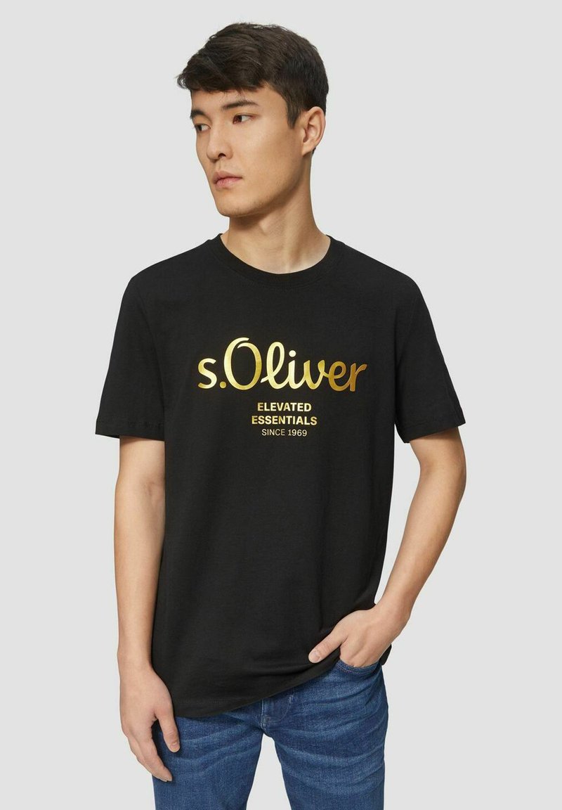 Black cotton t-shirt featuring gold lettering "s.Oliver" and "ELEVATED ESSENTIALS SINCE 1969" on the front, round neckline, short sleeves.