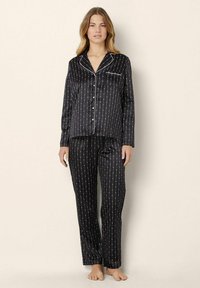 Zwart satijnen pyjamaset met een knoopsluiting bovenkant en lange broek. De stof heeft verticale witte strepen met kleine rode accenten.