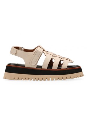 Beige lederen sandaal met een gekruisd bandontwerp, een dikke zwarte en beige zool en een gestructureerde afwerking; heeft een verstelbare hakband.