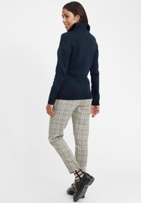 Navy knitted turtleneck sweater with ribbed cuffs, paired with gray and black plaid tapered trousers and black lace-up shoes.