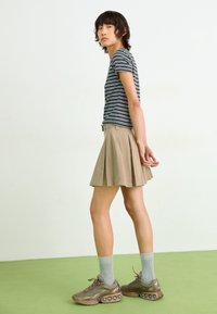 Striped short-sleeve shirt, beige pleated skirt, gray knee-high socks, and brown sneakers with bubble accents. Simple and casual outfit.