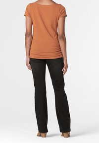 Camiseta marrón de manga corta, diseño ajustado y detalle fruncido en los laterales, combinada con pantalones negros de pierna recta y zapatos de tacón color beige.