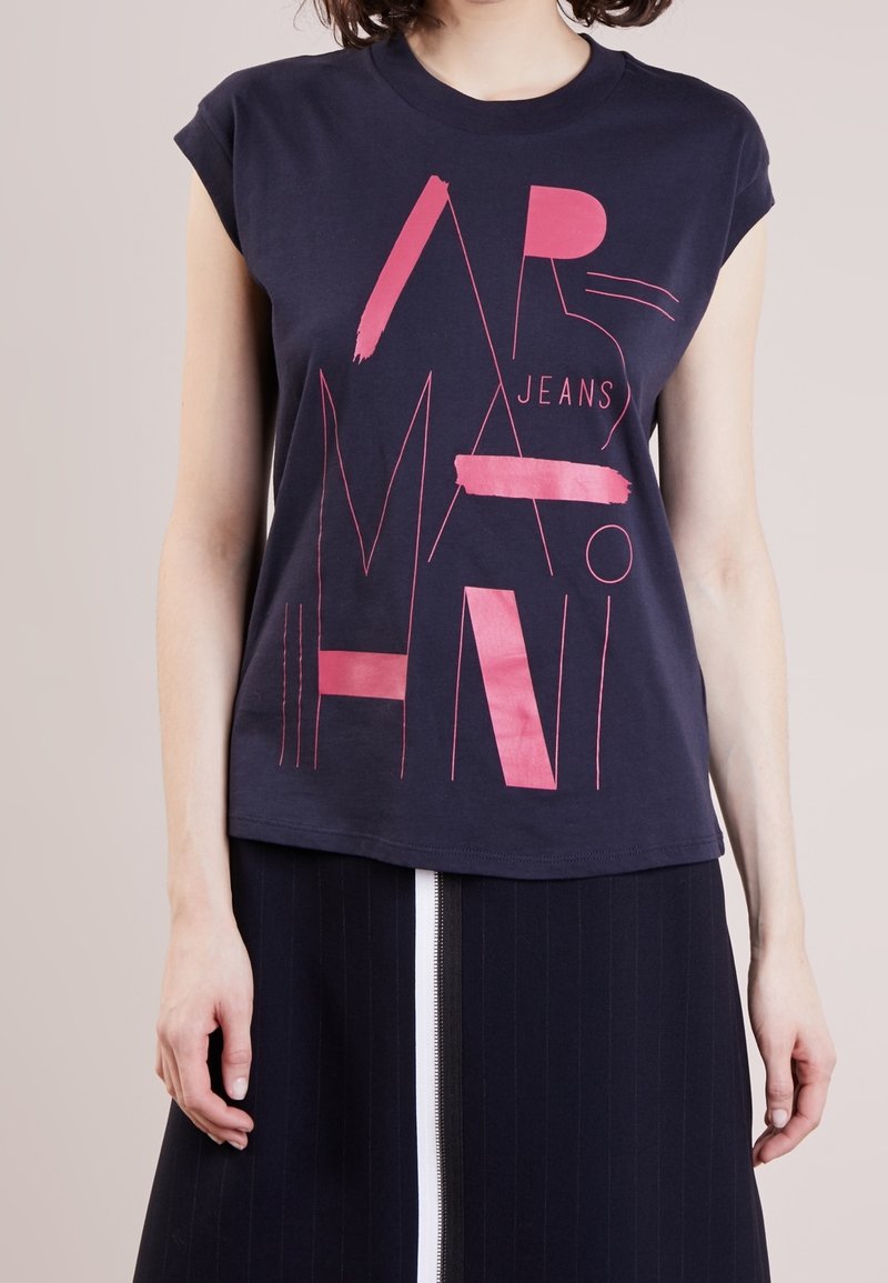 Námořnická modrá bavlněná tričko s krátkým rukávem, s výrazným růžovým grafickým textem a liniemi. Design je moderní a ležérní.