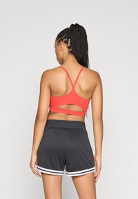 Κόκκινο αθλητικό στήθος με λεπτομέρεια κοψίματος στην πλάτη, συνδυασμένο με μαύρες βερμούδες που έχουν άσπρες ρίγες στο τελείωμα. Λείο και εφαρμοστό ύφασμα.