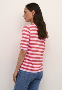 Randig stickad topp med växlande rosa och korall horisontella ränder, korta ärmar och rund halsringning. Bärs med blå jeans.