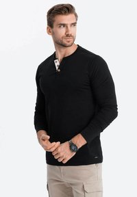 Schwarzes Langarm-Henley-Shirt mit Rundhalsausschnitt, drei weiße Knöpfe mit braunen Akzenten, taillierte Passform, glatte Textur.