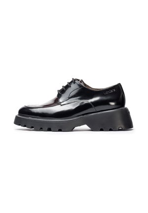 Zapato de charol negro con suela gruesa y estriada, y diseño de cordones. Presenta costuras en contraste y logotipo emblema en el talón.