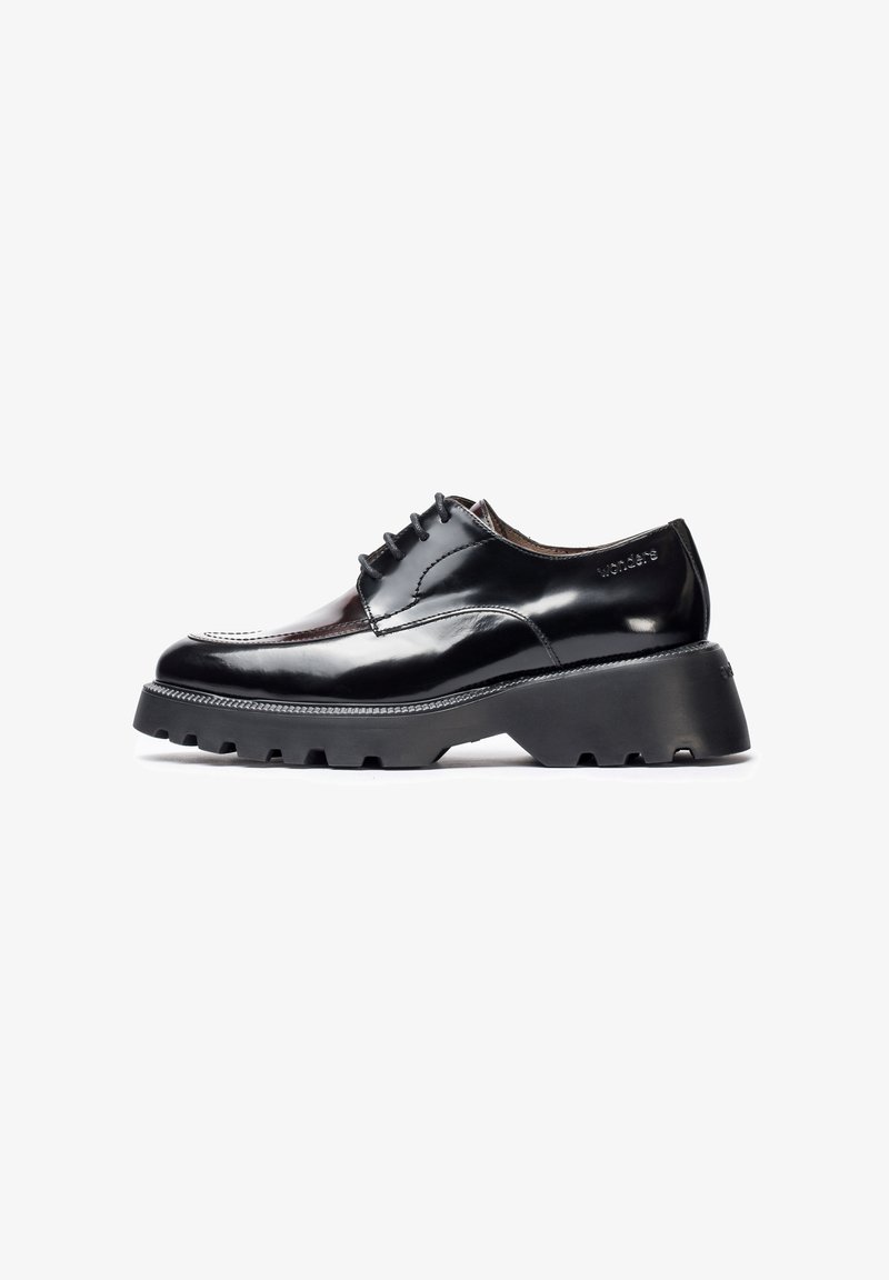 Zapato de charol negro con suela gruesa y estriada, y diseño de cordones. Presenta costuras en contraste y logotipo emblema en el talón.