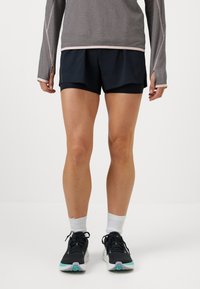 Čierne športové šortky s vrstveným dizajnom, ľahkým materiálom a elastickým pásom. V kombinácii s šedým dlhým rukávom a teniskami.