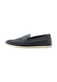Mocasines trenzados grises con una parte superior texturizada, ribete suave y suela blanca en contraste, con un diseño plano y sin herrajes visibles.