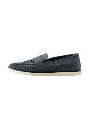 Grå vævede loafers med en struktureret overdel, glat kant og en kontrastfarvet hvid sål, der har et fladt design uden synligt hardware.