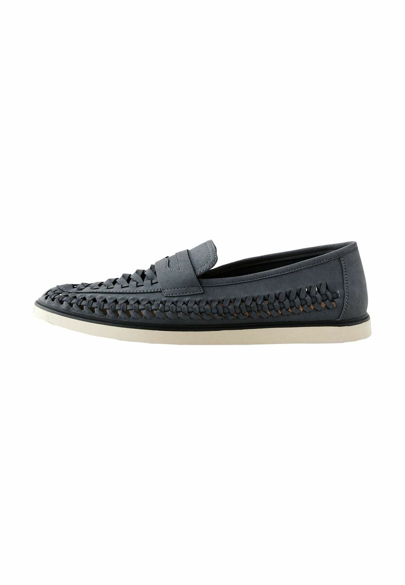 Mocasines trenzados grises con una parte superior texturizada, ribete suave y suela blanca en contraste, con un diseño plano y sin herrajes visibles.