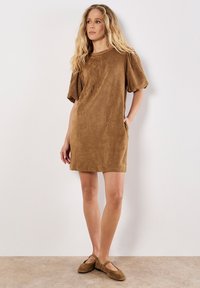 Robe courte en daim marron avec de courtes manches bouffantes, un décolleté rond et des poches latérales. Tissu lisse et texturé avec une coupe décontractée.