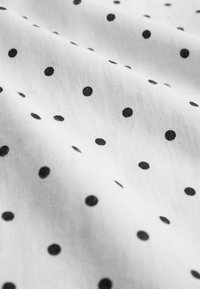 Bela tkanina z gladko teksturo je posuta s črnimi pikami različnih velikosti, kar ustvarja enostaven a izrazit vzorec.