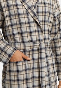 Rutig badrock i ljusblå, beige och marinblå med bälte, långa ärmar och sidofickor i ett mjukt, texturerat tyg.