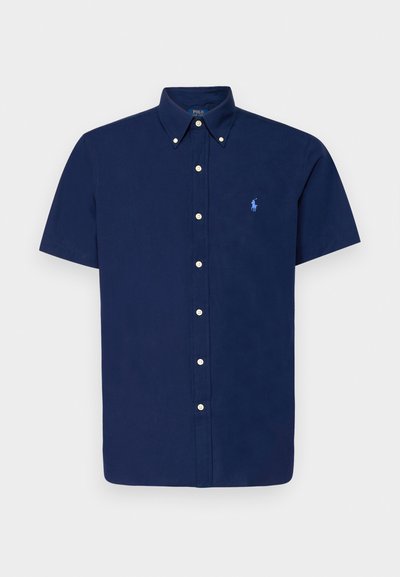 Granatowa koszula z krótkim rękawem zapinana na guziki, z wyostrzonym kołnierzykiem i małym, jasnoniebieskim logo polo. Posiada białe guziki oraz gładki, teksturowany materiał.