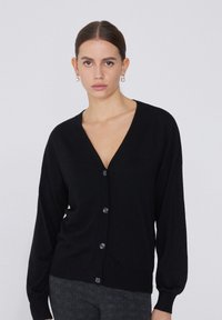 Schwarze Strickjacke mit tiefem V-Ausschnitt, langen Ärmeln und Knopfleiste. Weicher Stoff mit gerippten Bündchen, ausgestattet mit großen, dunklen Knöpfen.