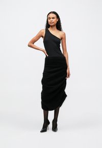 Top preto de um ombro só, com uma saia preta drapeada e texturizada. A modelo veste sapatos de salto altos pretos e meias pretas transparentes. Design simples e moderno.