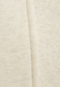 Bijela pletenina s mekom, teksturiranom površinom; vidljivi rebrasti uzorci i blage varijacije u boji dodaju dubinu materijalu.