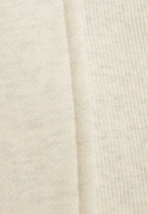 Tissu tricoté blanc avec une surface douce et texturée ; des motifs côtelés visibles et de légères variations de couleur ajoutent de la profondeur au matériau.