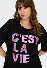 Camiseta negra con gran texto de lentejuelas rosas "C'EST LA VIE". Mangas cortas, escote redondeado y un corte relajado. Tela de textura suave.