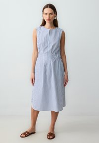 Blau-weißer, gestreifter ärmelloser Kleid mit rundem Ausschnitt, tailliertem Bund und knielangem Rock. Getragen mit braunen flachen Sandalen.