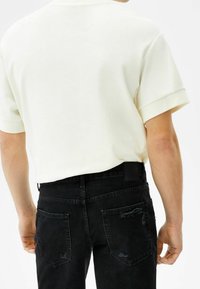 Košile s krátkým rukávem v krémové barvě vyrobená z měkké látky, doplněná černými džínami z denimu s opotřebovanou texturou a dvěma zadními kapsami.